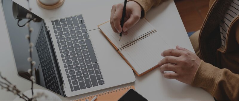 Mann schreibt auf Notizblock vor eienm PC