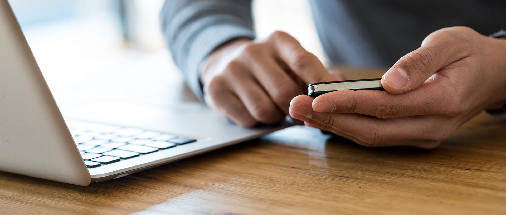 Mann am Laptop lässt sich von Smartphone ablenken