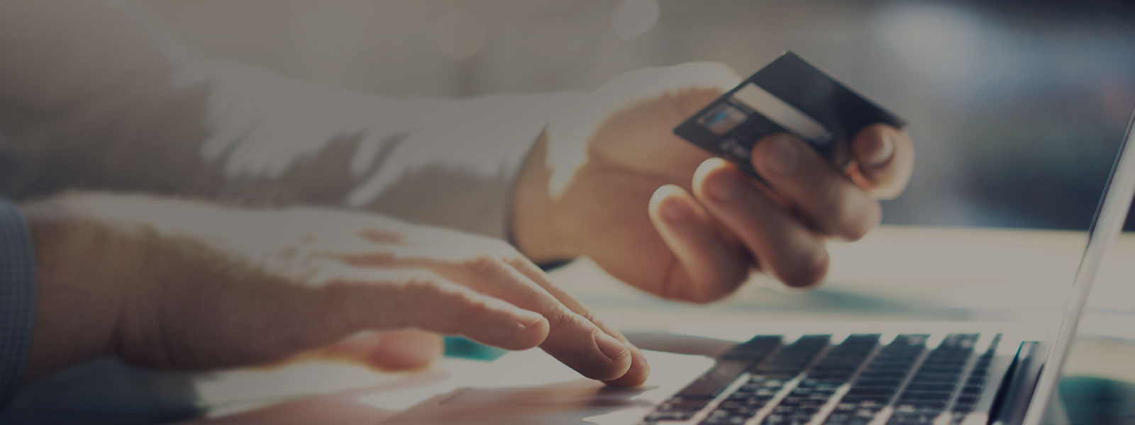 Header Mann hält Bankkarte in der Hand und bedient Laptop